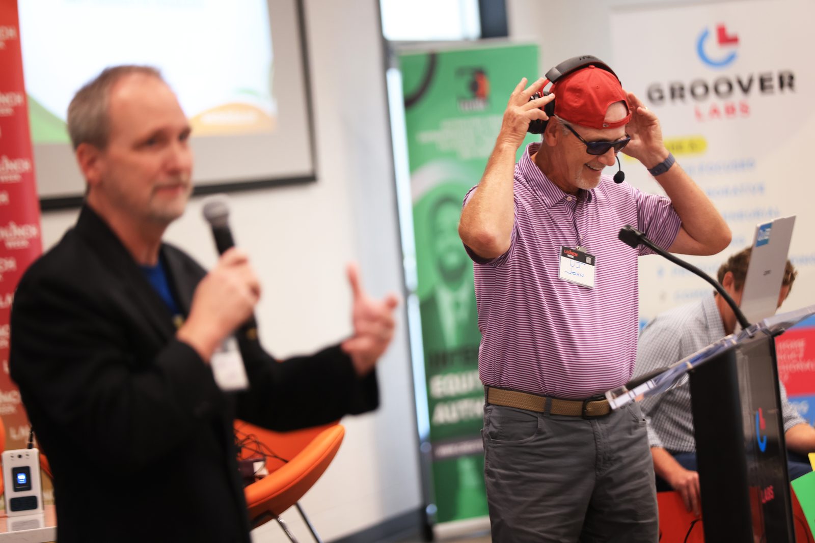 An attendee in a red cap and sunglasses grinning while trying on a headset, mid-demo.