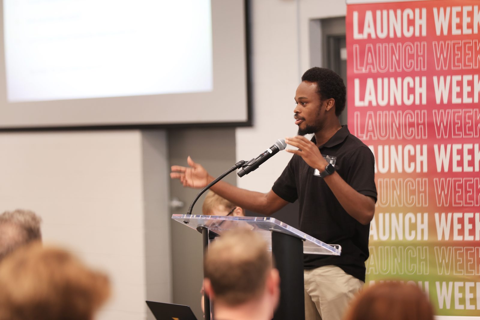 A builder presenting at the podium in front of a Launch Week banner.
